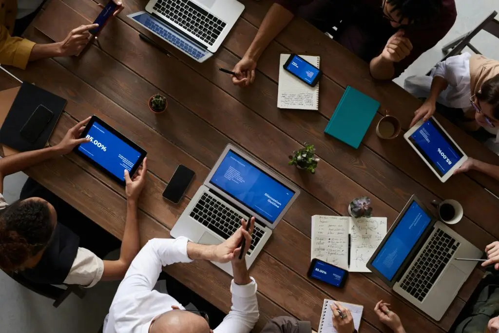 pexels-photo-3183183-3183183 Overhead view of a diverse team discussing around a wooden table, using technology.
